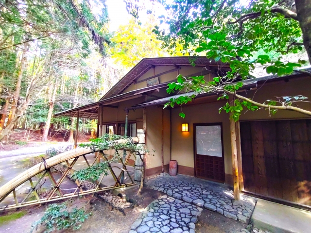 椿大神社の境内にある茶室の外観。竹の橋と石畳、木々に囲まれた自然豊かな環境の中に佇む建物。