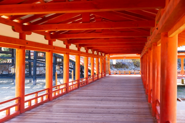 厳島神社の朱塗りの回廊。木製の床と赤い柱が並び、奥へと続いている様子が印象的。