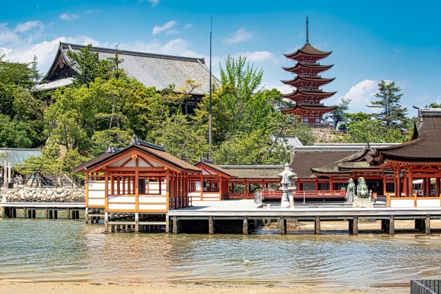 海に浮かぶ厳島神社の社殿と、背景にそびえる五重塔。緑の木々と青空に包まれた景観が広がる。