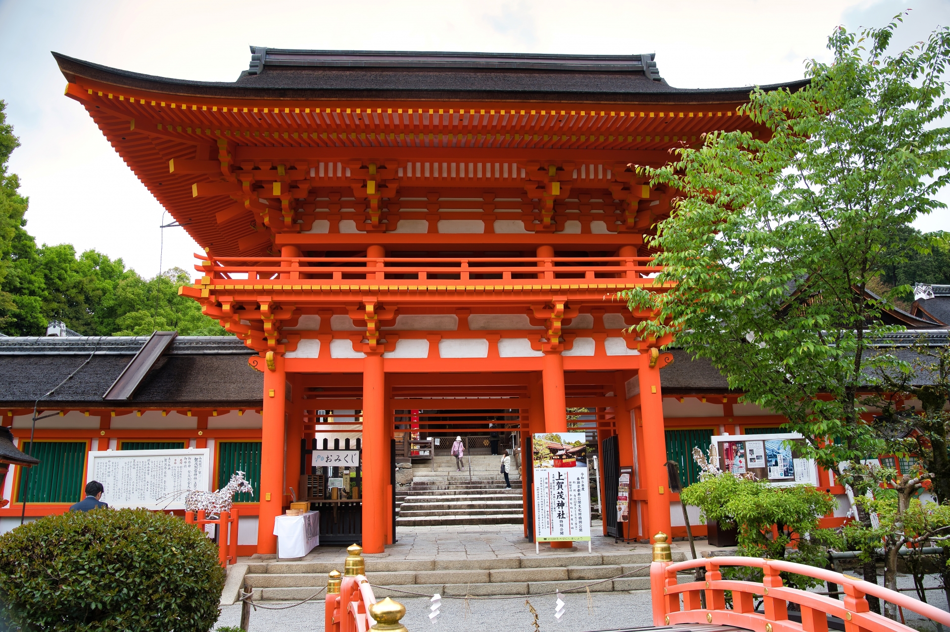 朱色の上賀茂神社楼門の正面写真。左右に木々があり、中央奥には石段が続く。