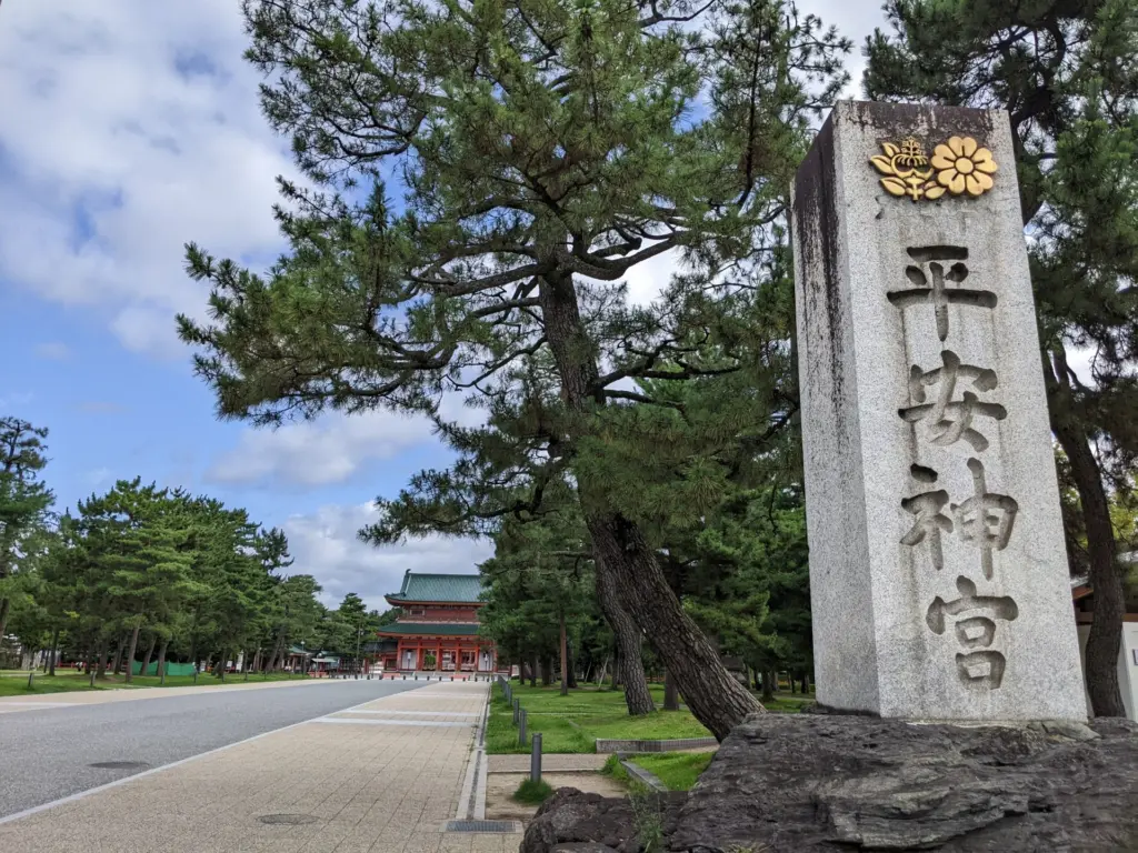 平安神宮の石碑と参道。松林と青空の中、朱塗りの社殿が奥に見える。