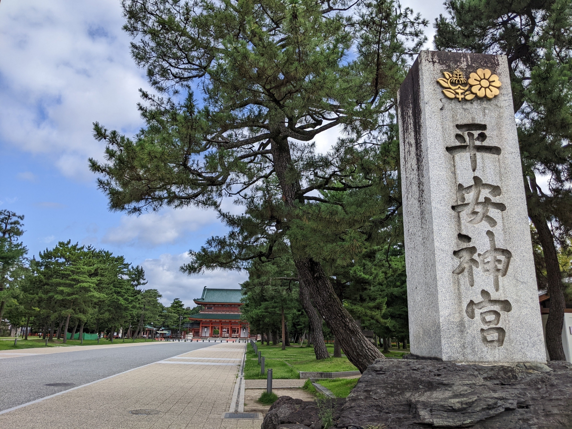 京都 縁結び 神社 おすすめ 神宮の石碑と参道。松林と青空の中、朱塗りの社殿が奥に見える。