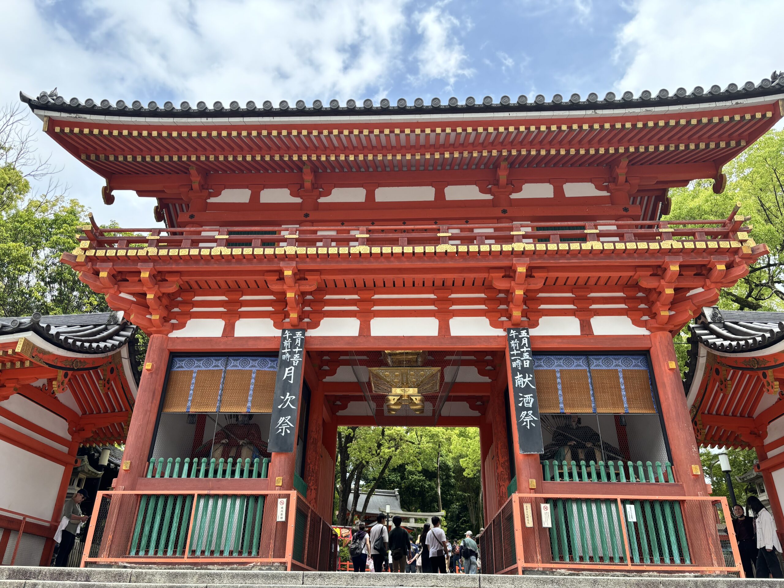 八坂神社 縁結び パワースポット八坂神社の朱色の楼門（西楼門）を正面から撮影した写真。多くの参拝者が出入りし、5月5日の祭事案内板が掲示されている。