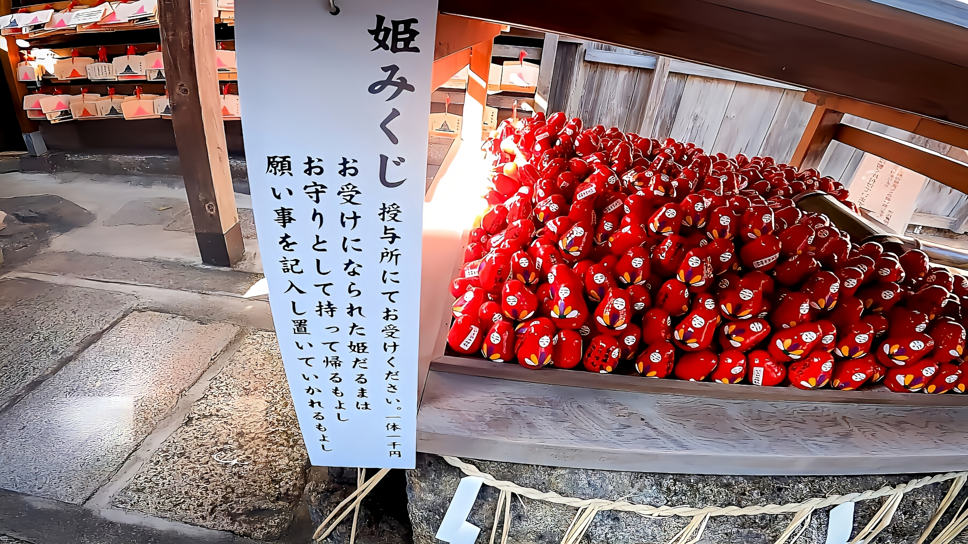 市比賣神社の姫みくじ。赤い姫だるまが並ぶ奉納所と、説明書きの立て札。縁結びや願掛けで人気のお守り型みくじ。